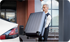 Chauffeur VTC Paris aidant à charger une grande valise dans le coffre d'une voiture, symbolisant la prise en charge complète du client.